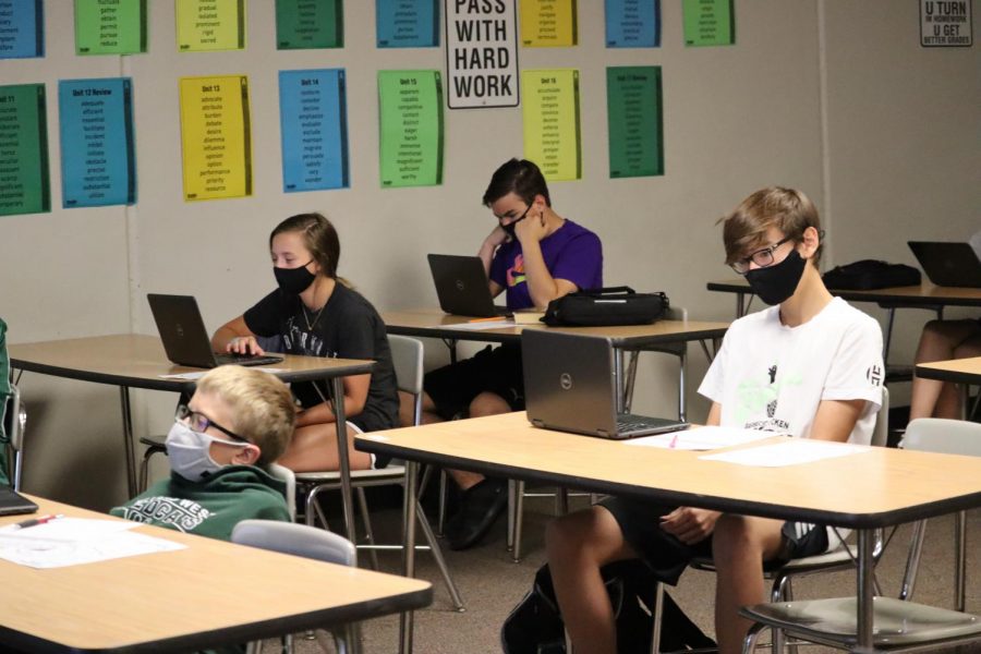 Students in room 131 learn on their computers while they are in person. Every student is wearing a mask. 