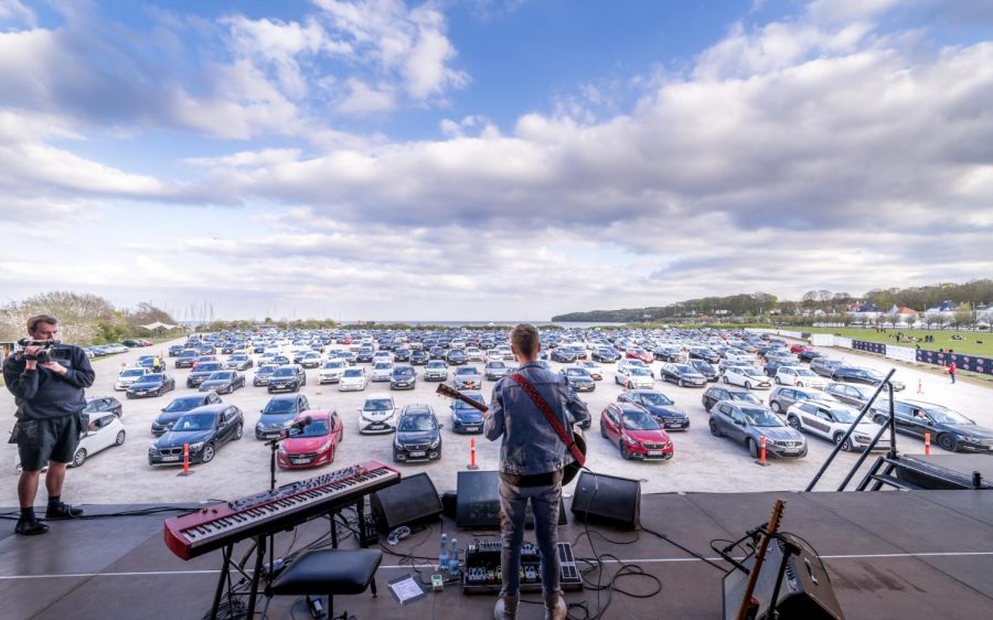 Cars lined up and distanced from each other at the new outdoor venue in Denmark show another way people can safely enjoy live music. People at the concert are able to connect to a private FM radio station so that they can hear the performer in their car. 
