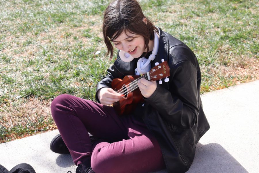 Sitting on the cement outside, junior Chloe Brandenburg strums a song on the ukulele as they sing along with the music. Brandenburg has recently taken up the hobby of playing the ukulele again and shares their music during lunch. “It makes me feel really happy when people listen to me at lunch,” Chloe Brandenburg said. “I am very good at trashing on myself, so it’s a welcome change.”
