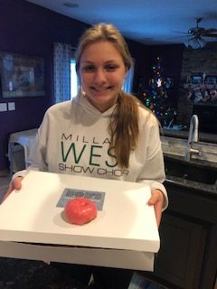 Junior Campbell Macy stands holding a box of the donuts that she designed. On the top of the box, there is a donut with red hot frosting. “We turned the cinnamon candy into a very thick syrup and emulsified that into our standard white icing,” Bob’s Donuts chef Keri Tull said. “We already had an apple cake donut that we were selling so we used that. The toppings are a syrup that we made and crushed cinnamon candy.” 
