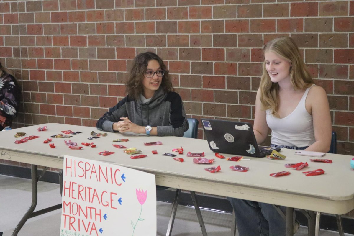 Junior+Gabriela+Witmer+%28left%29+and+senior+Zoe+Dykes+%28right%29+spend+their+lunch+hour+manning+the+SHHs+trivia+booth.+We+have+some+tabs+here+with+trivia+questions+about+hispanic+history%2C+Witmer+said.+If+you+get+one+right%2C+you+get+a+piece+of+candy.