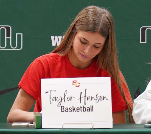 Looking down at a paper, senior Taylor Hansen signs her letter of intent. Hansen was signing to play division three womens basketball. I chose Simpson College in Iowa, Hansen said. Their program really stood out to me because the coaches and players invited me in and welcomed me like I was a part of their family.
