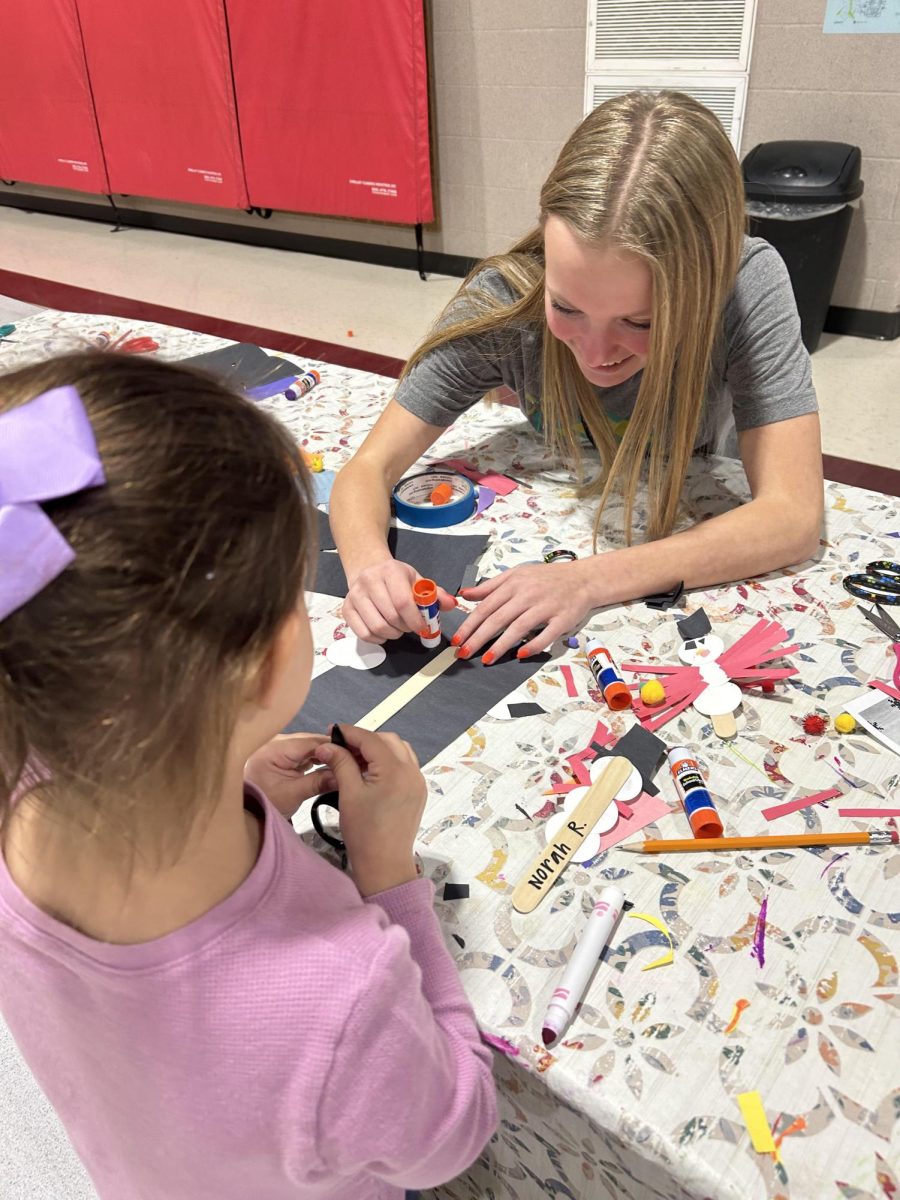 Gluing down a circle to make a snowman craft, junior Chloe Teter helps a kindergartener. Almost every day, Teter leads an art craft and helps the elementary school students when they need it. I really like to help with the craft when I can, Teter said. My favorite thing is to make the art along with them because we all hang them up on the wall together.
